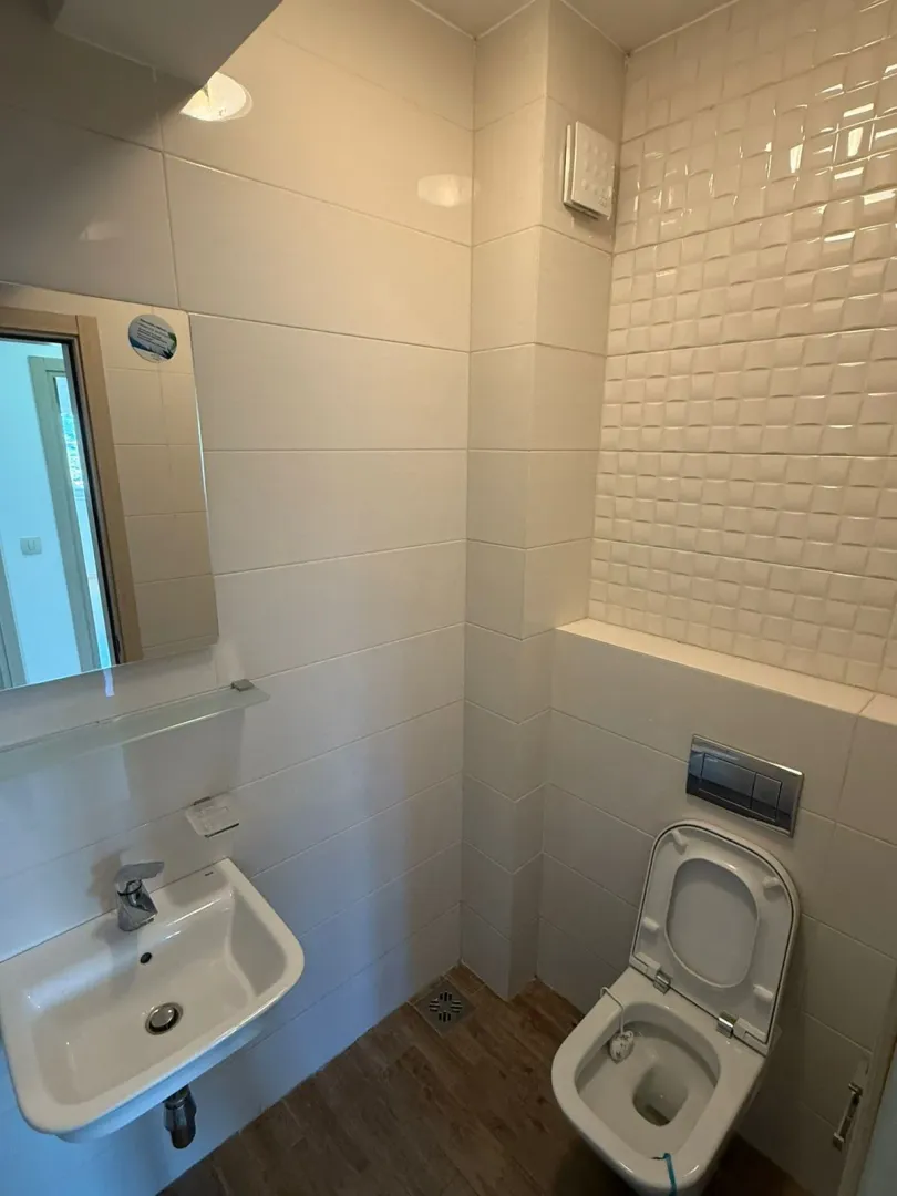 Manje kupatilo sa bijelim pločicama, umivaonikom i wc šoljom.
