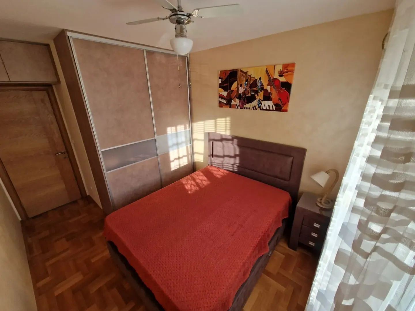 Namještena spavaća soba sa bračnim krevetom, plakarom i slikom na zidu.