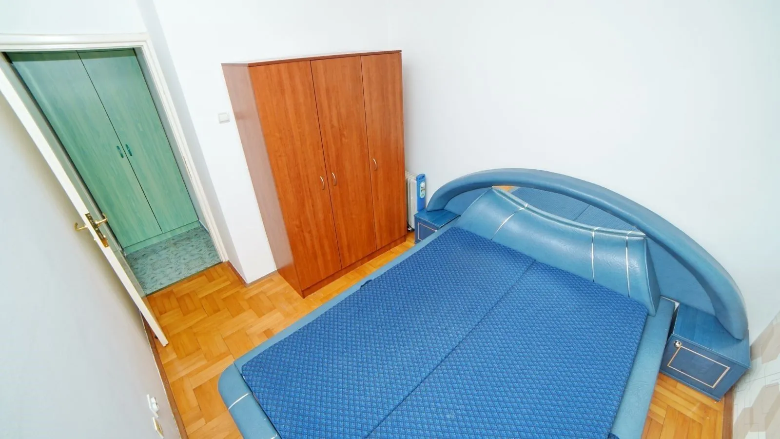A bedroom with a large blue bed and a wooden wardrobe.