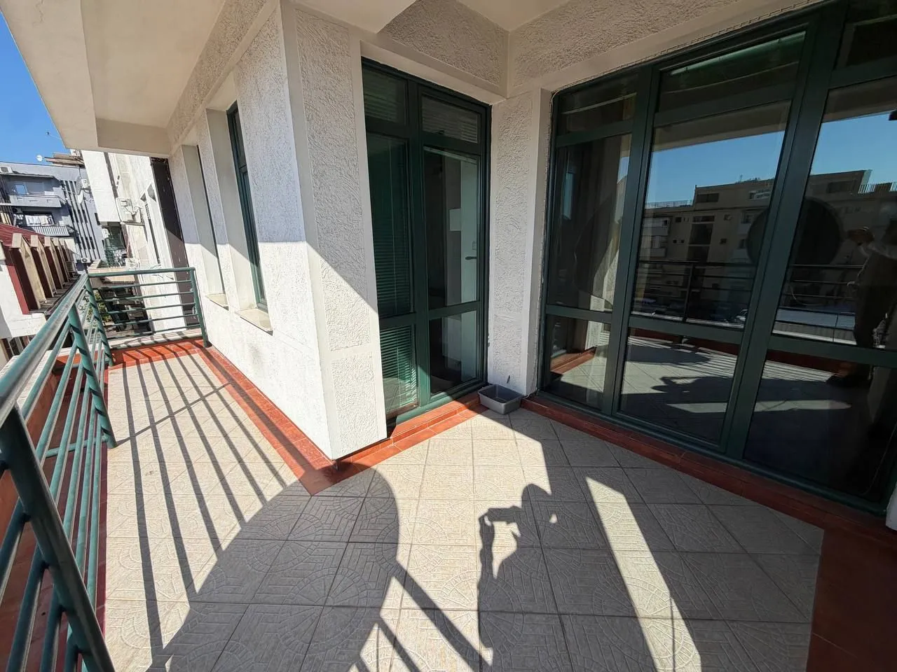 Spacious tiled terrace with a railing and large glass openings.