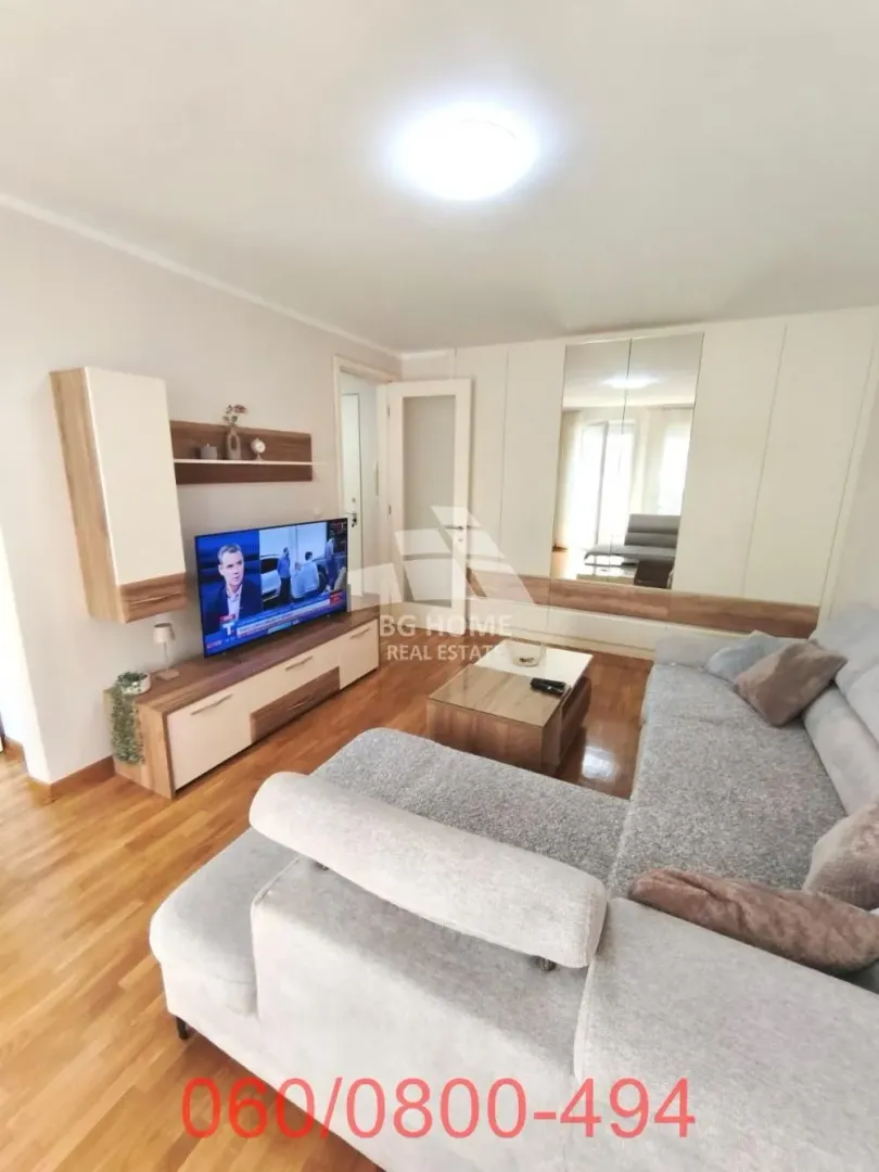 Dnevna soba sa ugaonom garniturom, televizorom i ugradnim plakarom.