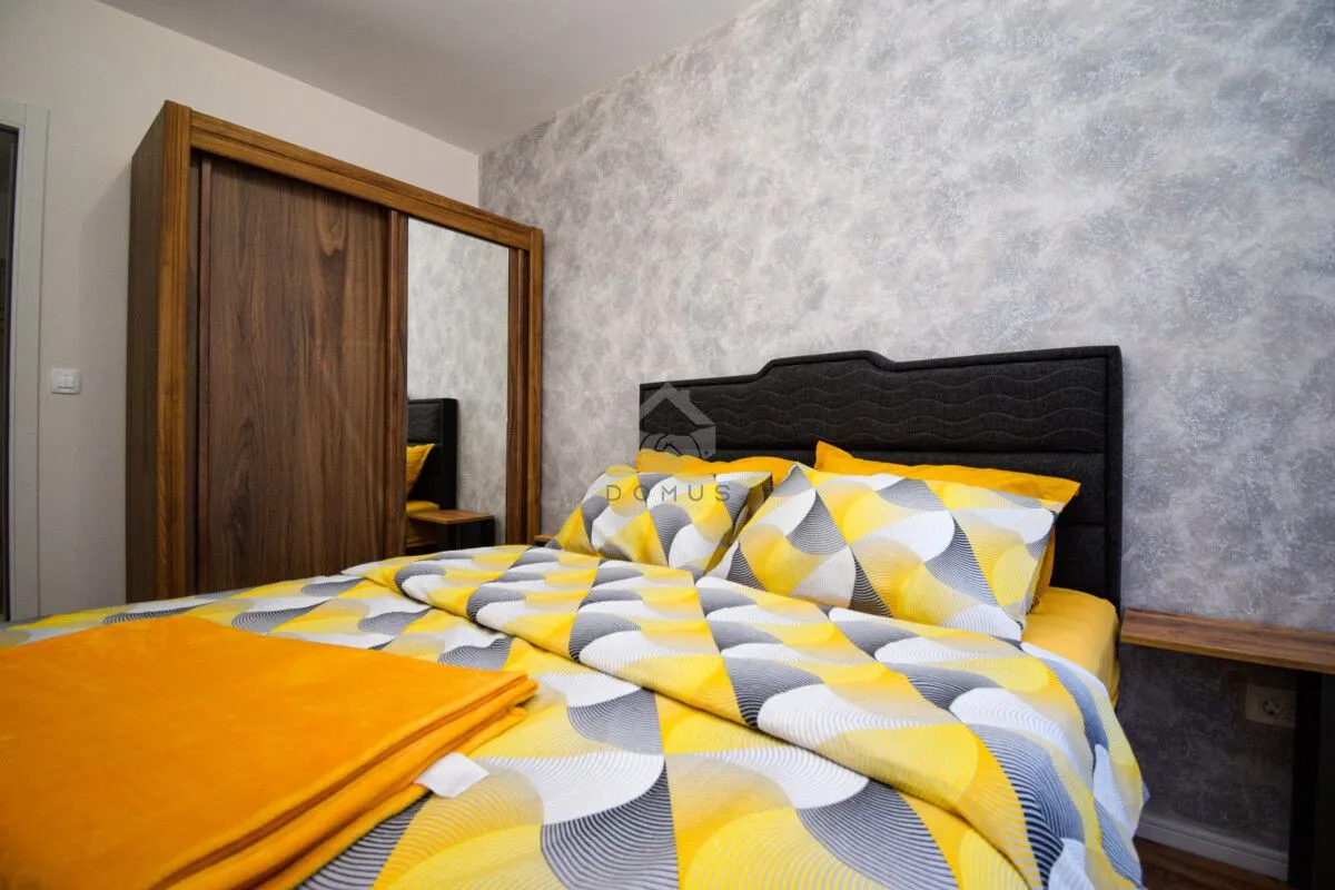 Bedroom with a double bed, wooden wardrobe with a mirror, and patterned bedding.