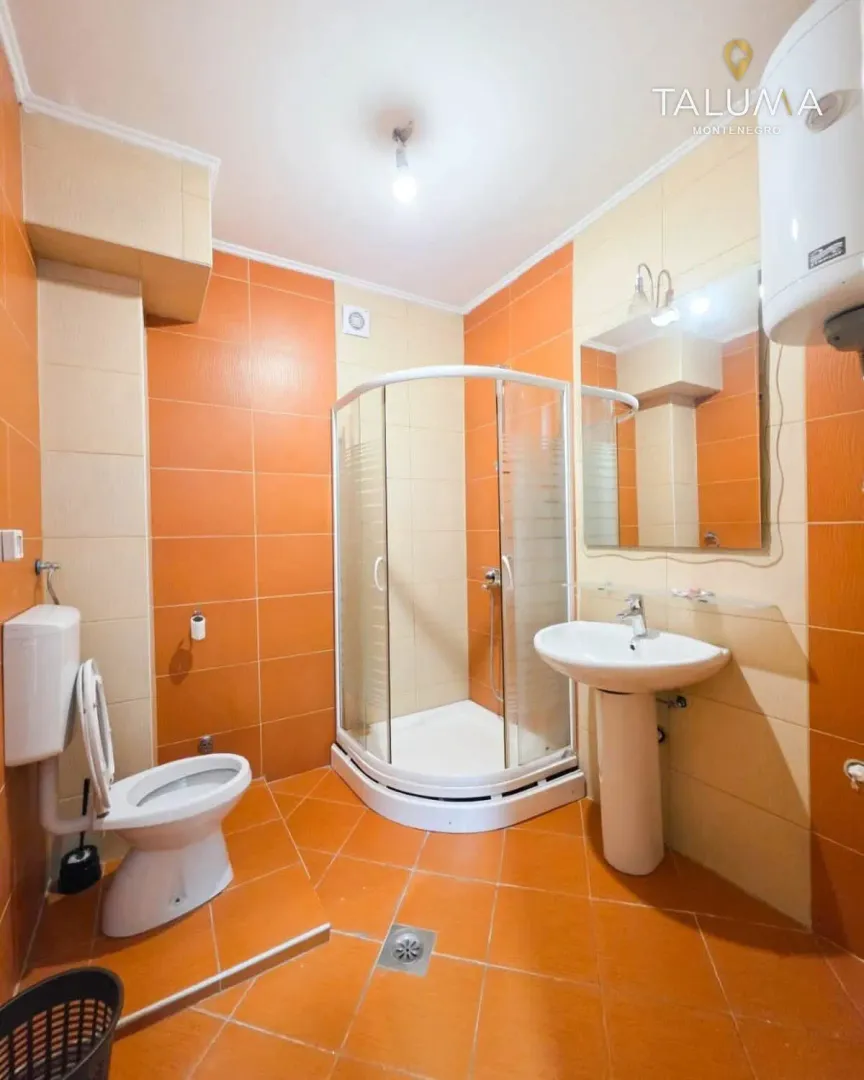 Kupatilo opremljeno tuš kabinom, umivaonikom, ogledalom i WC šoljom.