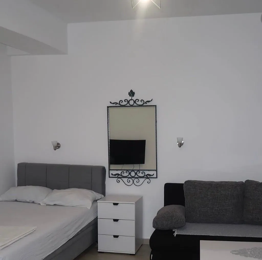 Spavaća soba sa bračnim krevetom, noćnim stočićem i ogledalom na zidu.