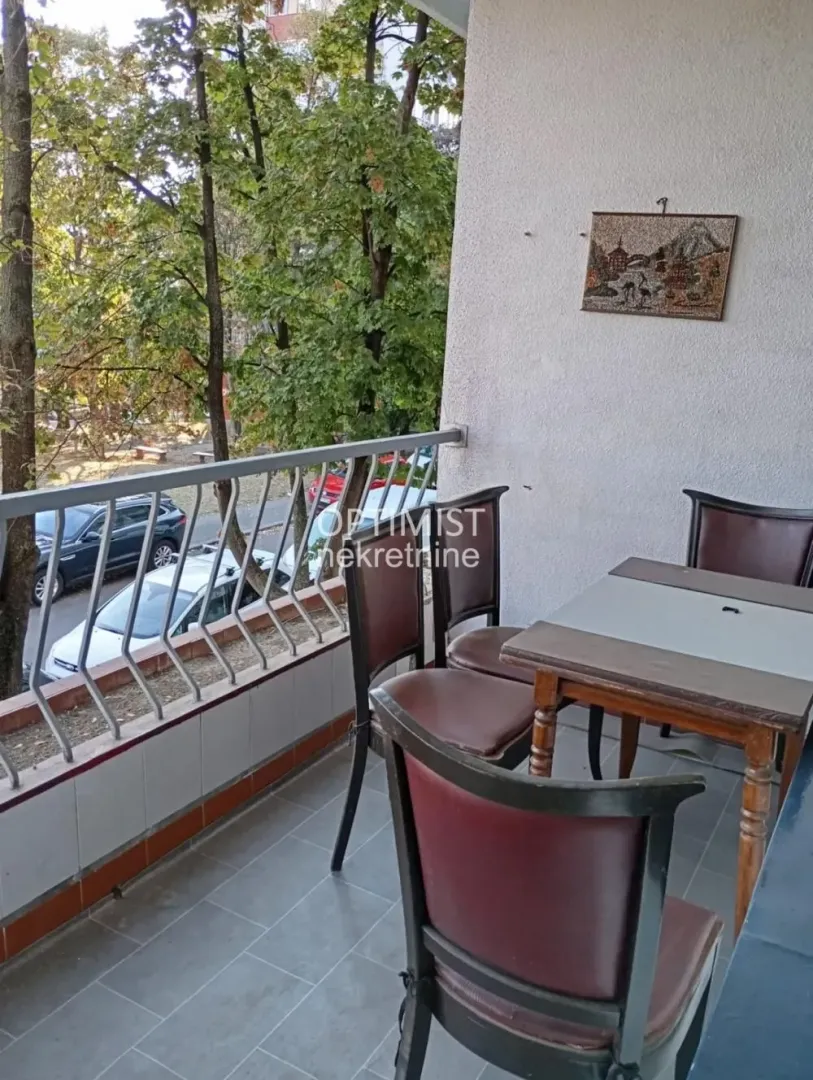 Namešten balkon sa trpezarijskim stolom i stolicama i pogledom na zelenilo.
