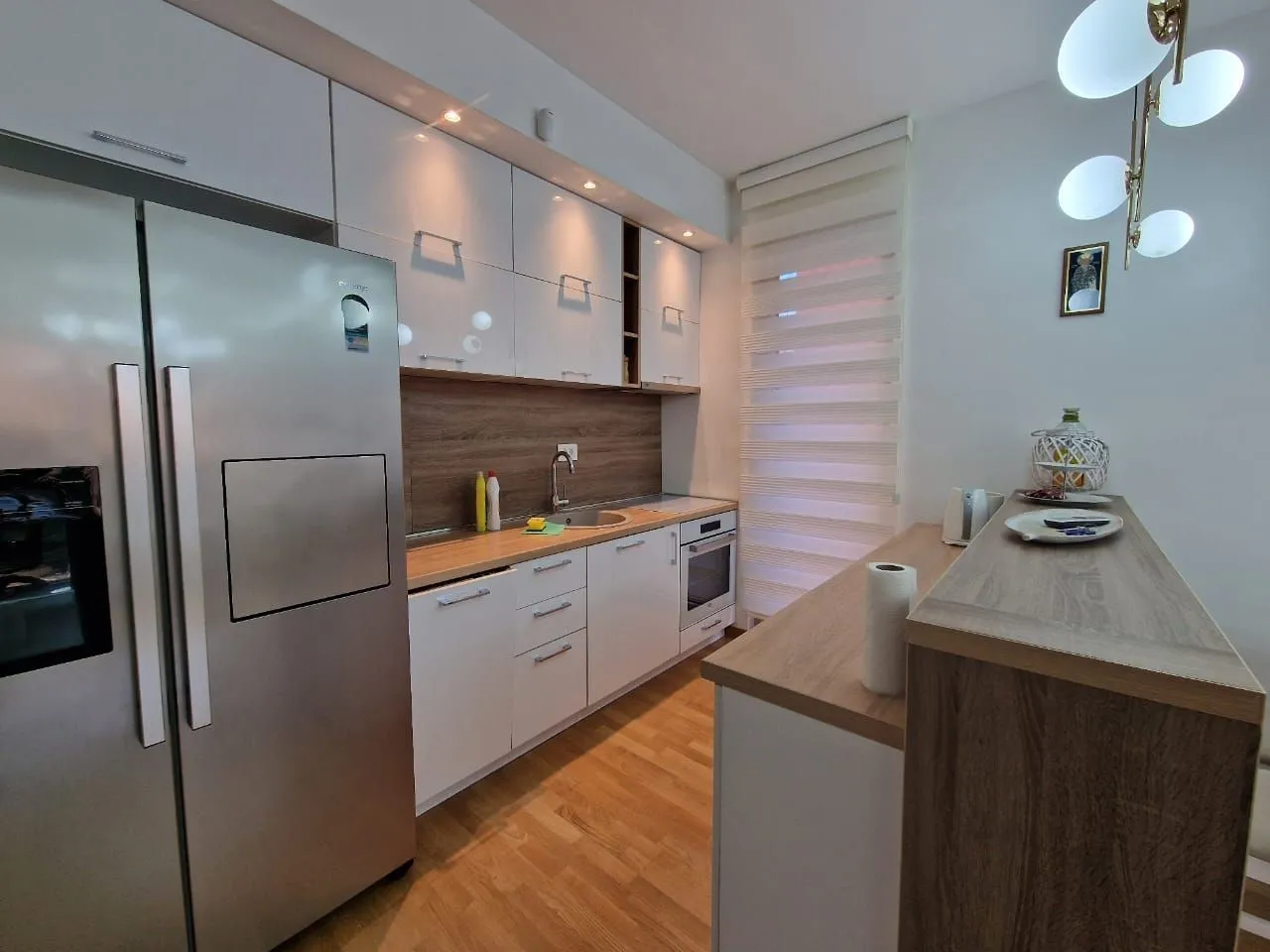 Modern kitchen with white cabinets, a large refrigerator, and a wooden breakfast bar.