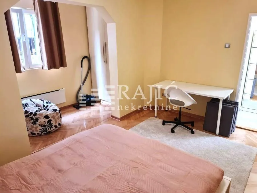 Furnished bedroom with a bed, desk, and parquet flooring.