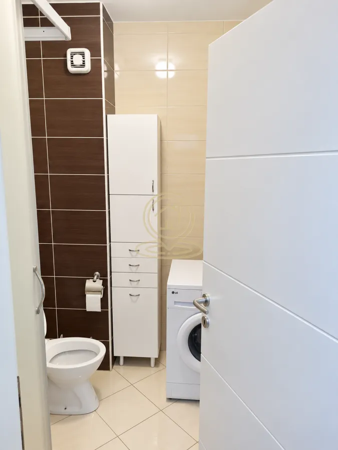 Kupatilo opremljeno toaletom, visokim ormarićem i mašinom za veš.