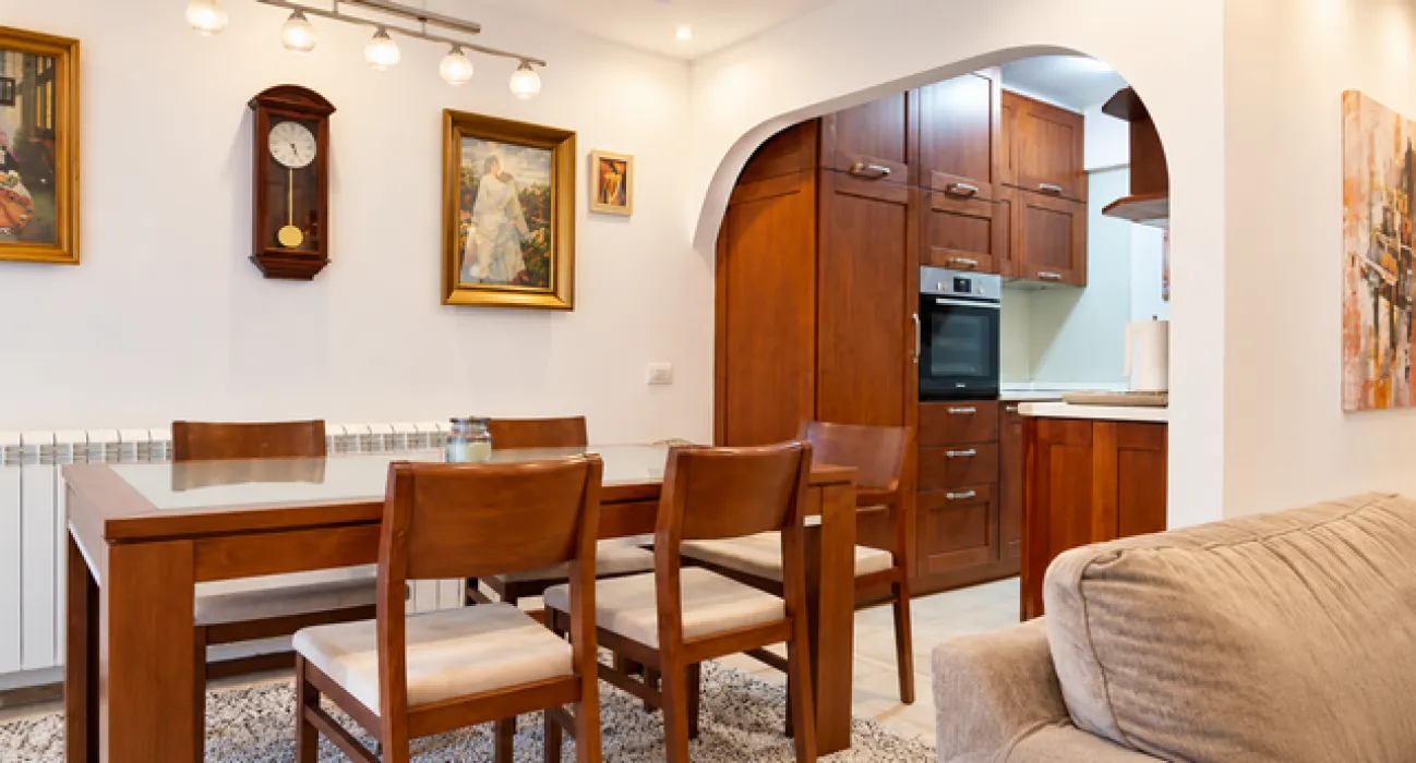 Dining area with a wooden table and chairs, with a view of the kitchen.
