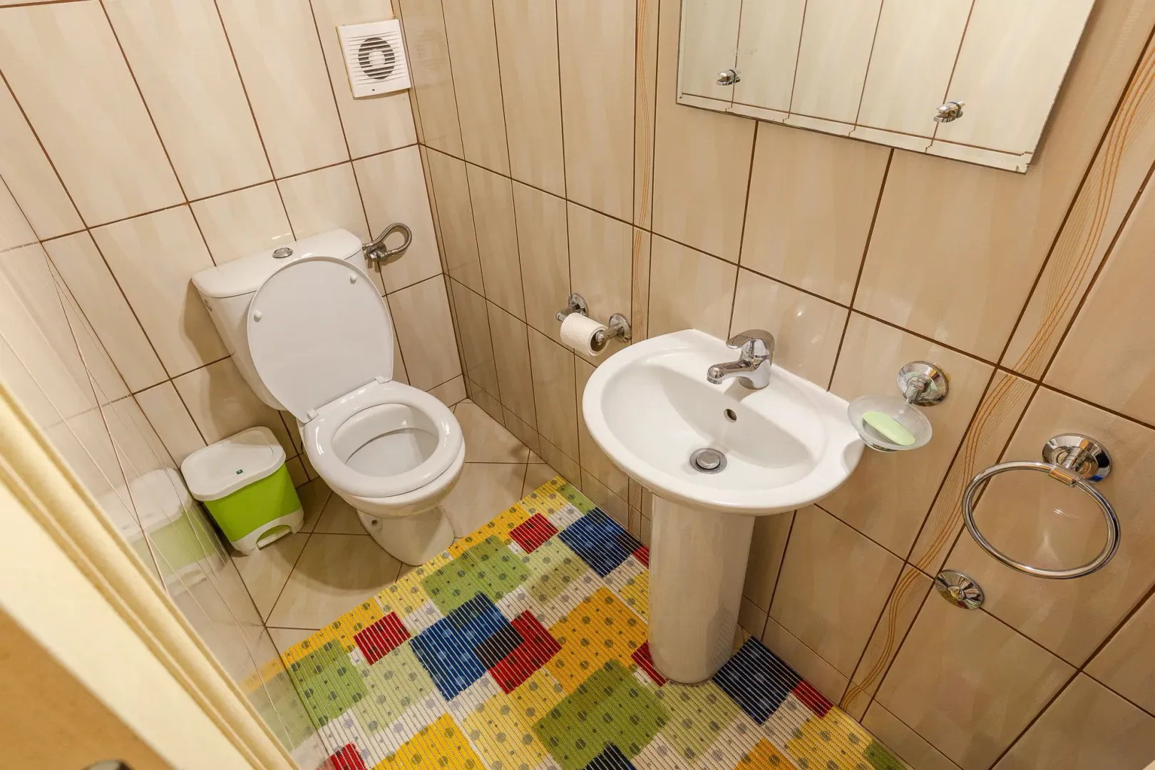 Manje kupatilo sa WC šoljom, umivaonikom i pločicama u bež tonovima.