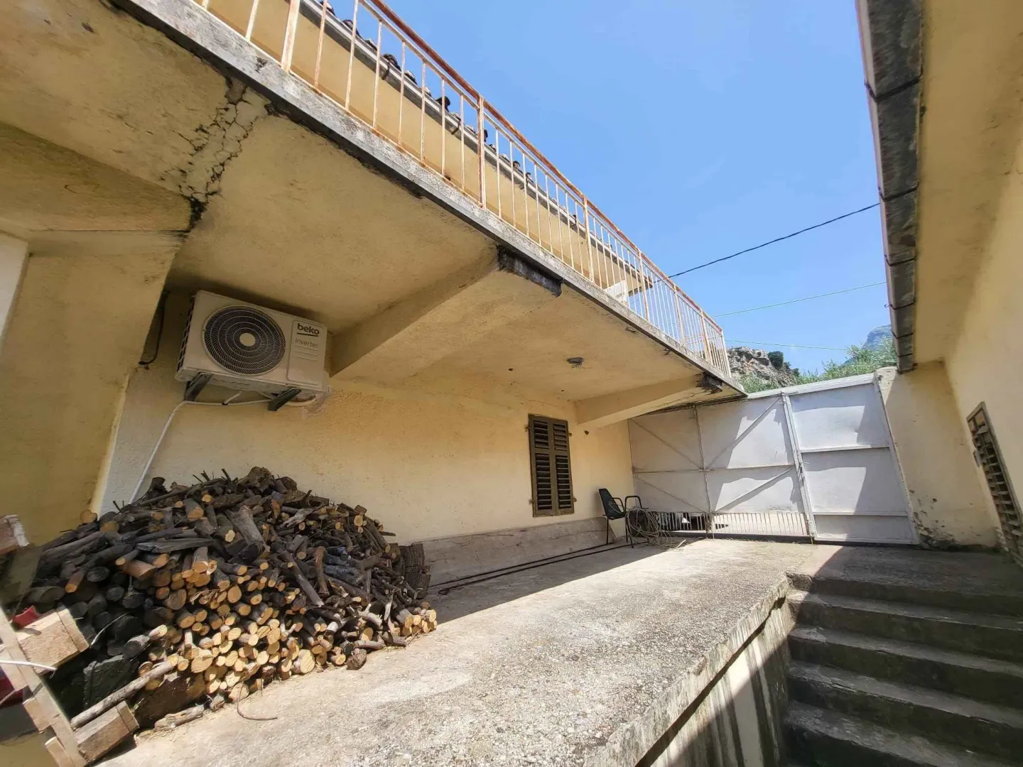 Spoljašnji dio kuće sa nadstrešnicom i složenim drvima za ogrijev.
