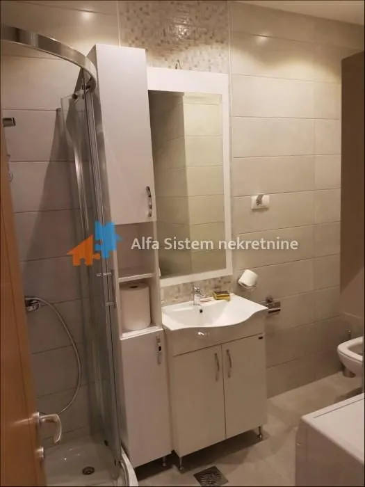 Kupatilo opremljeno tuš kabinom, umivaonikom sa ormarićem i ogledalom.
