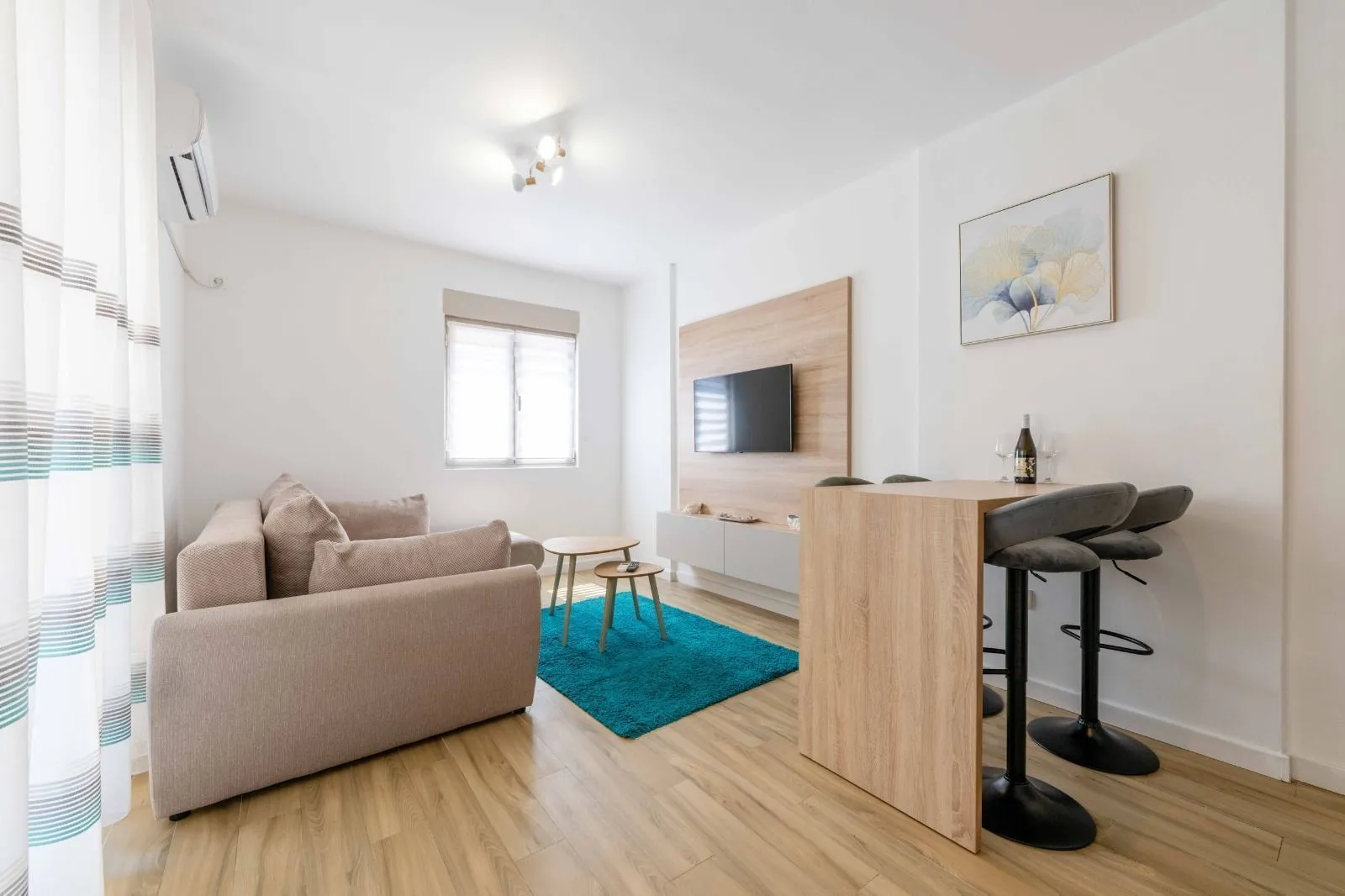 Living room with a sofa, TV, and a dining table with bar stools.