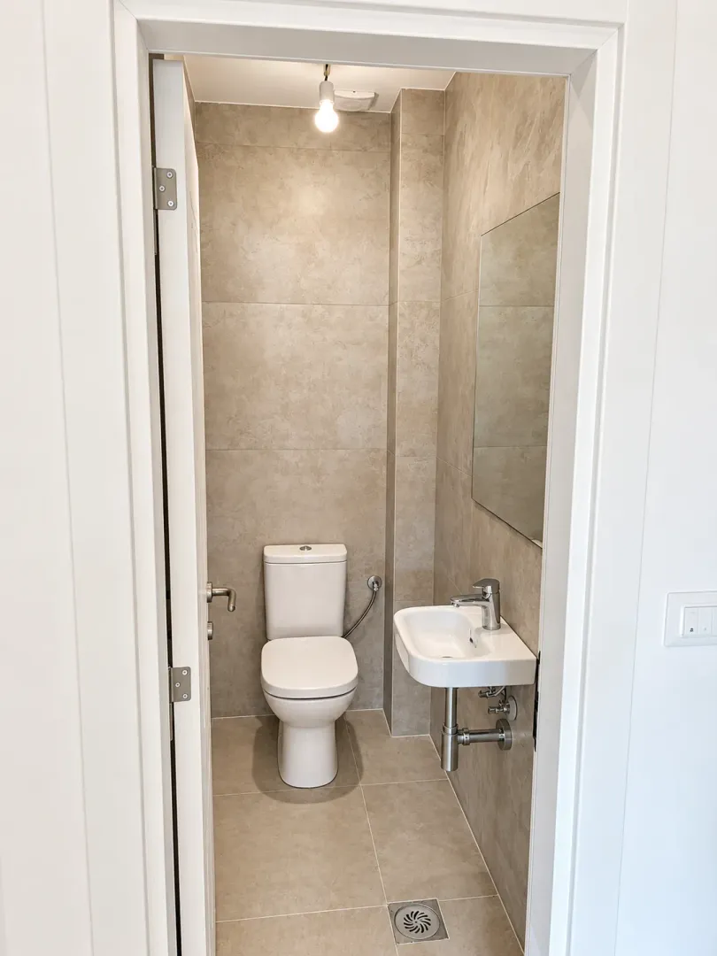Pogled iz predsoblja na manje kupatilo sa WC šoljom i umivaonikom.