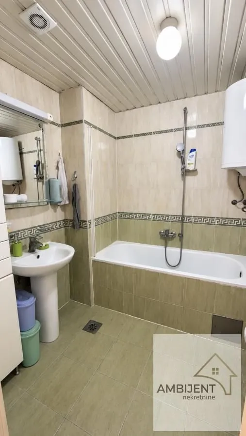 Kupatilo sa kadom, umivaonikom i pločicama u bež i zelenim tonovima.