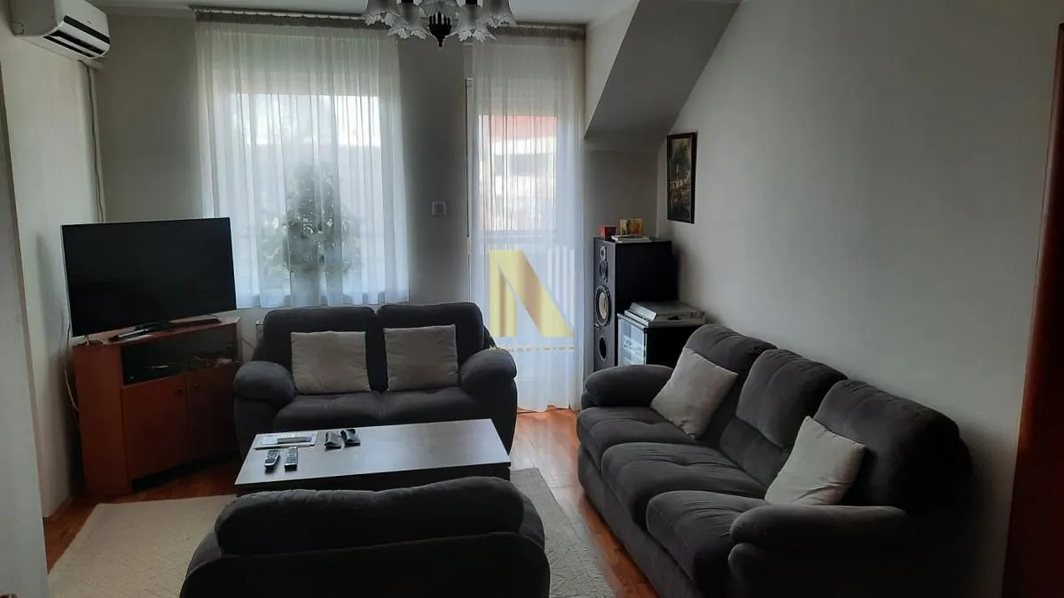 Dnevna soba sa garniturom za sedenje, televizorom i izlazom na terasu.