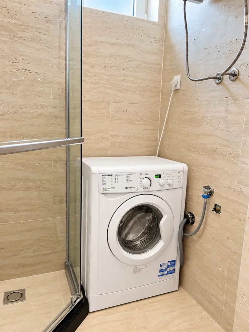 Bathroom with a glass shower enclosure and a washing machine, tiled in beige.