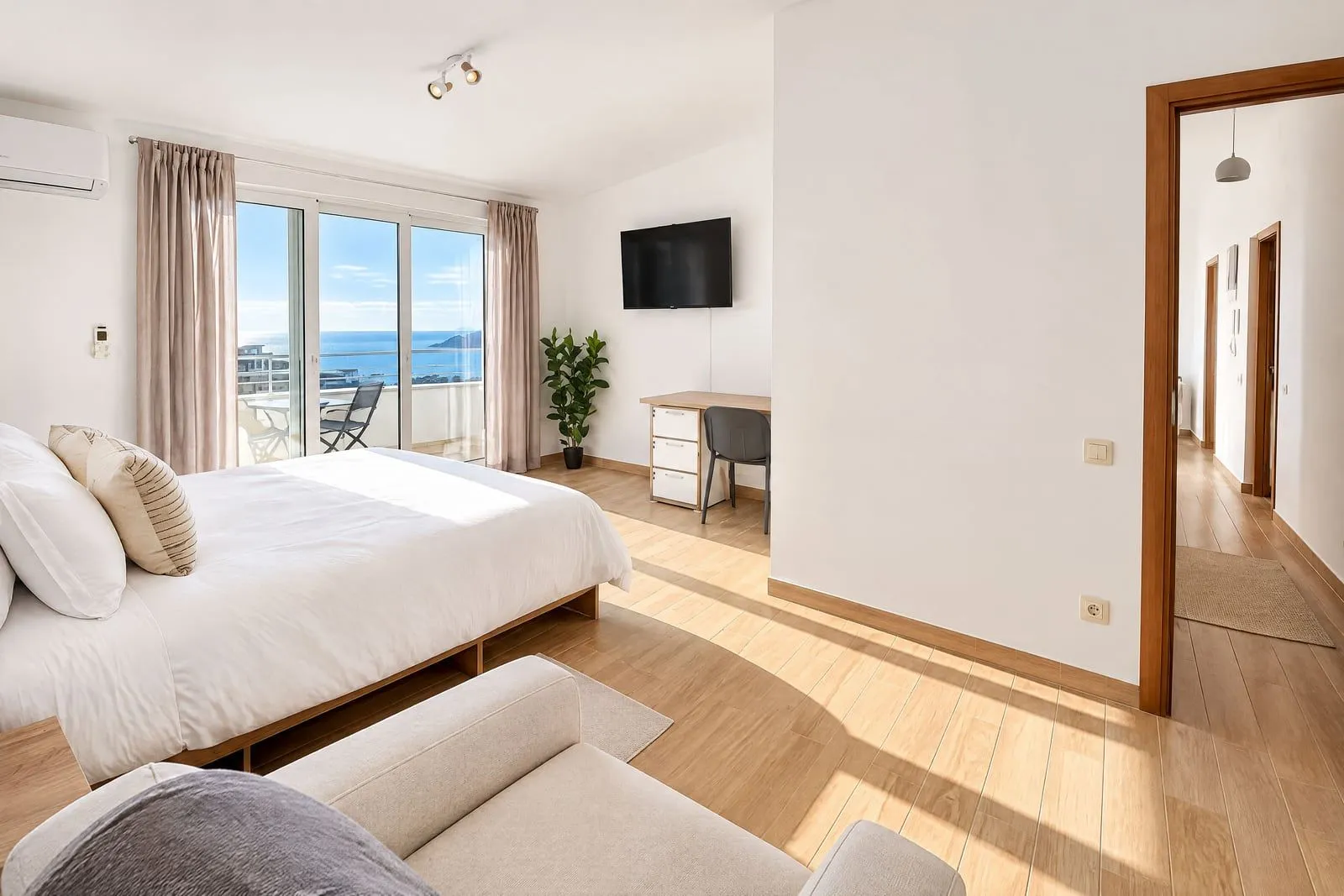 Spacious bedroom with a double bed, desk, and access to a terrace with a sea view.