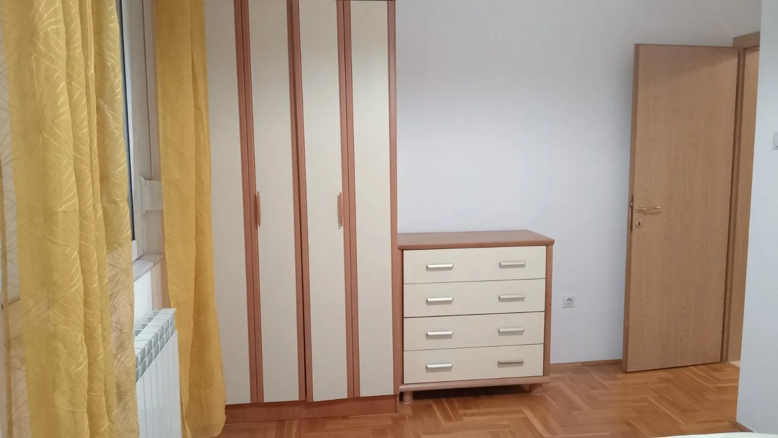 Bedroom interior with a wardrobe, chest of drawers, and yellow curtains.