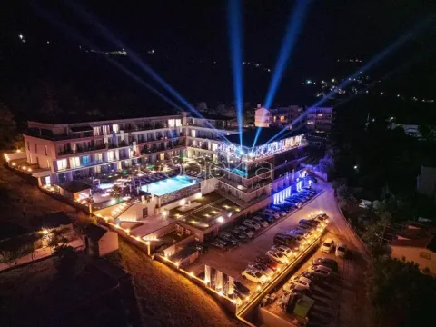 Noćni snimak iz vazduha prikazuje osvijetljeni hotelski kompleks sa bazenom i parkingom. - image 7