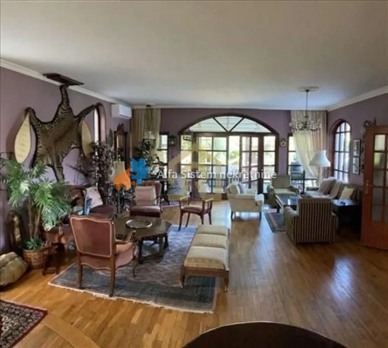 Spacious living room with seating furniture, wooden flooring, and large glass doors.