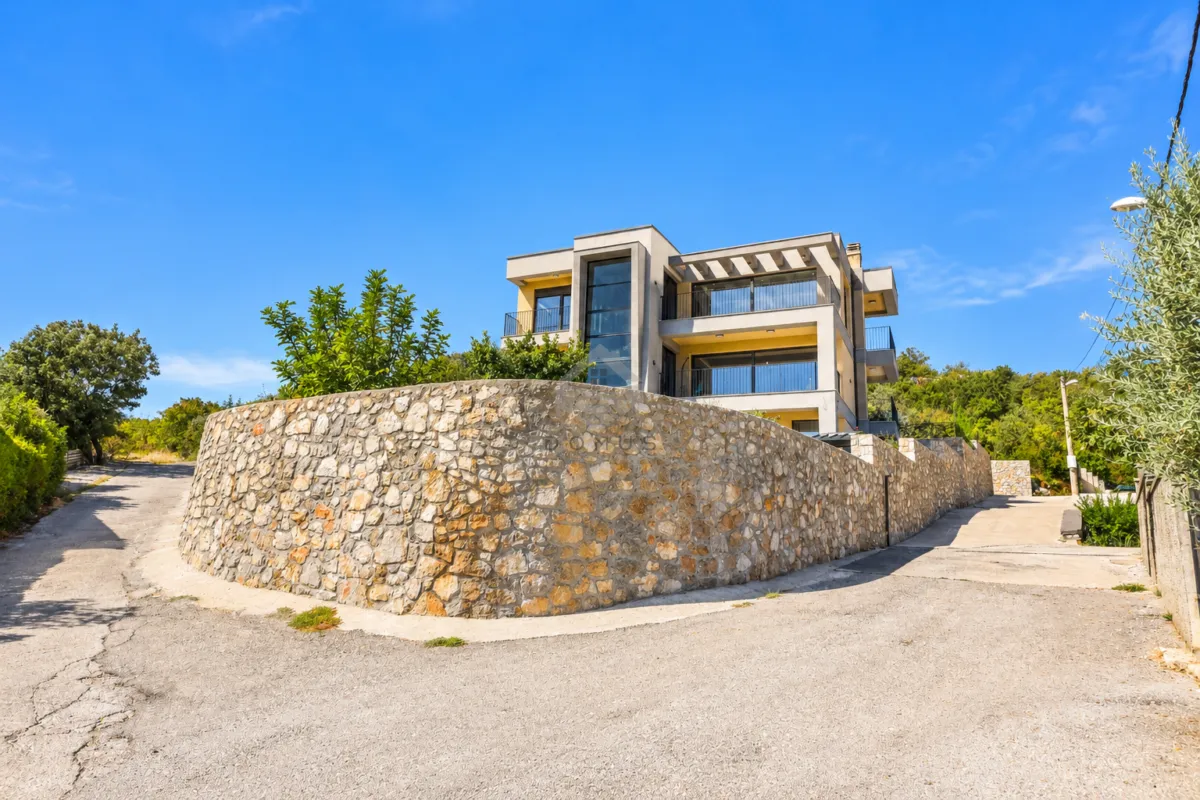 Exterior view of a modern multi-story house with a stone wall in the yard.
