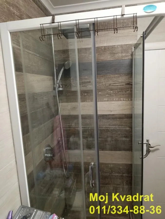 Kupatilo sa tuš kabinom i zidom obloženim pločicama u dezenu drveta.
