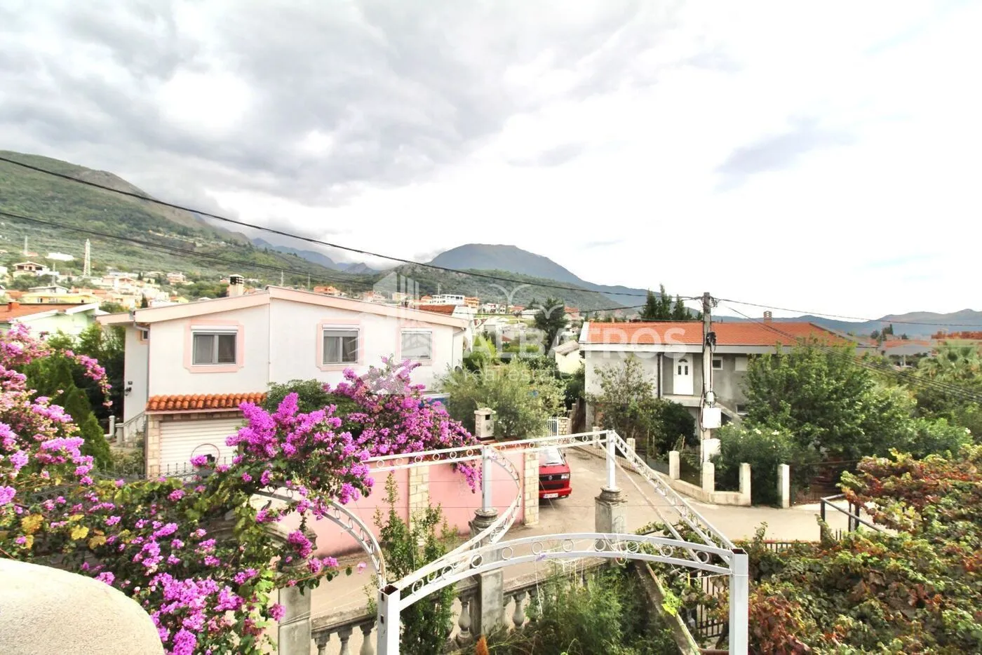 Pogled sa terase na okolne kuće i planine u pozadini.