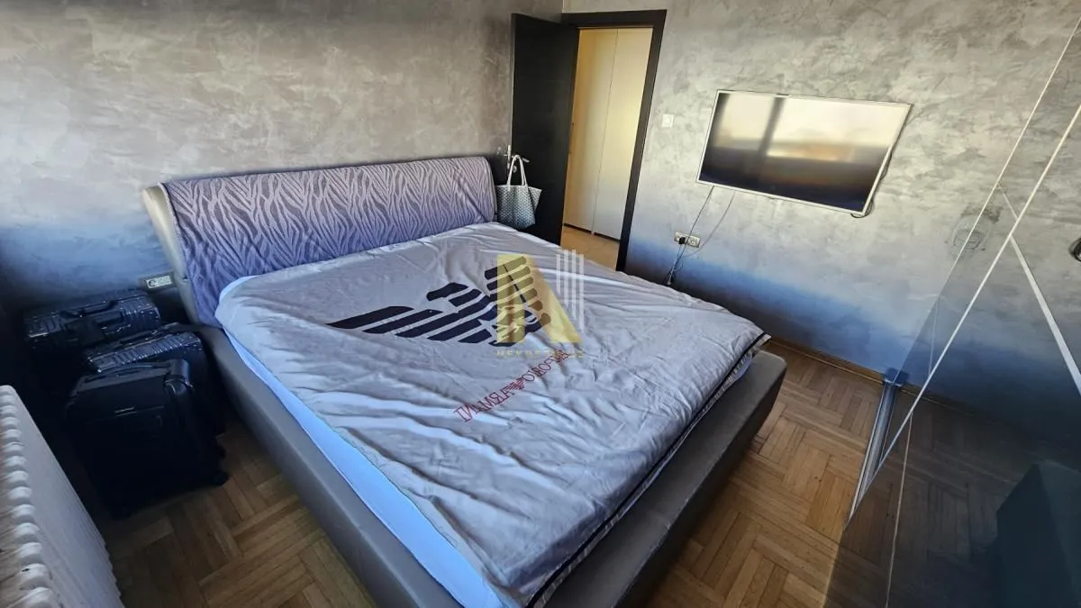 Nameštena spavaća soba sa bračnim krevetom, TV-om i parketom na podu.
