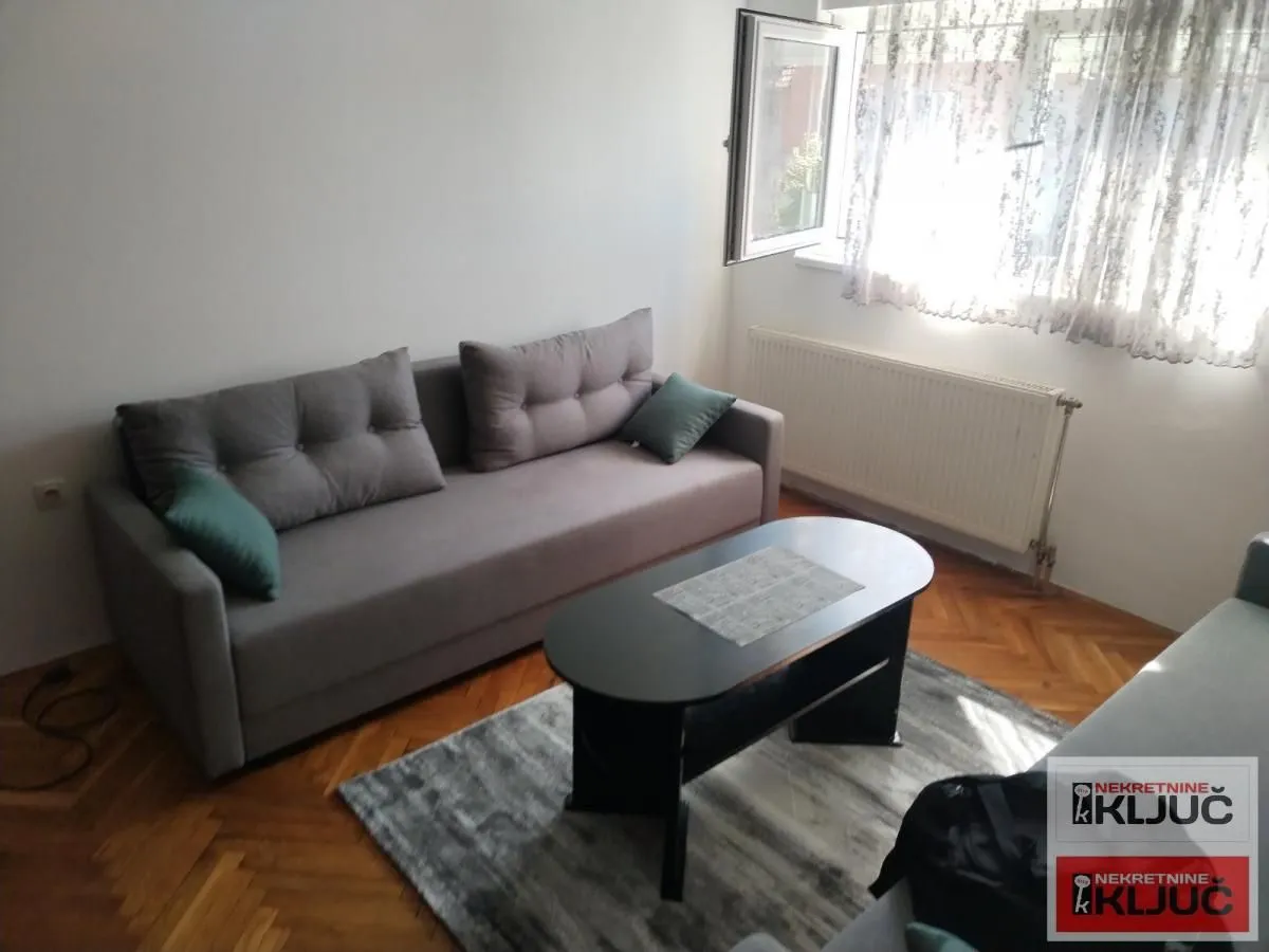 Dnevna soba sa sivom sofom, stočićem i prozorom.