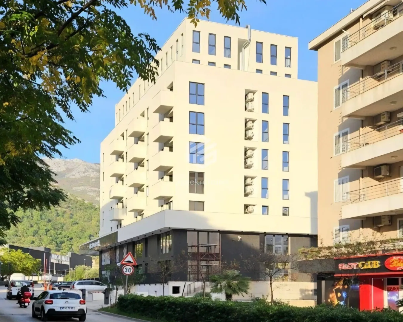 Pogled na spoljašnjost moderne stambene zgrade sa balkonom i okruženjem.