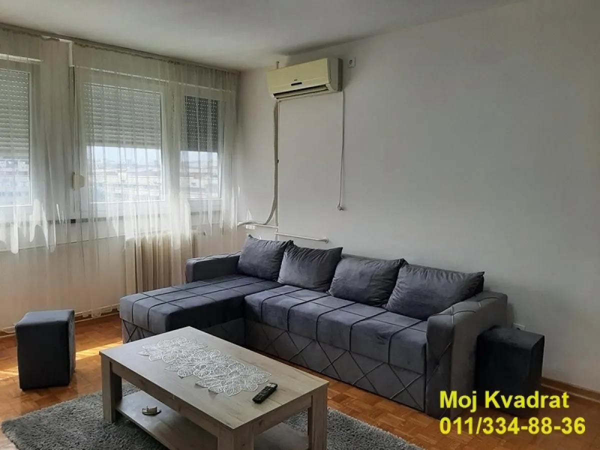 Living room with a corner sofa, coffee table, and air conditioning unit.