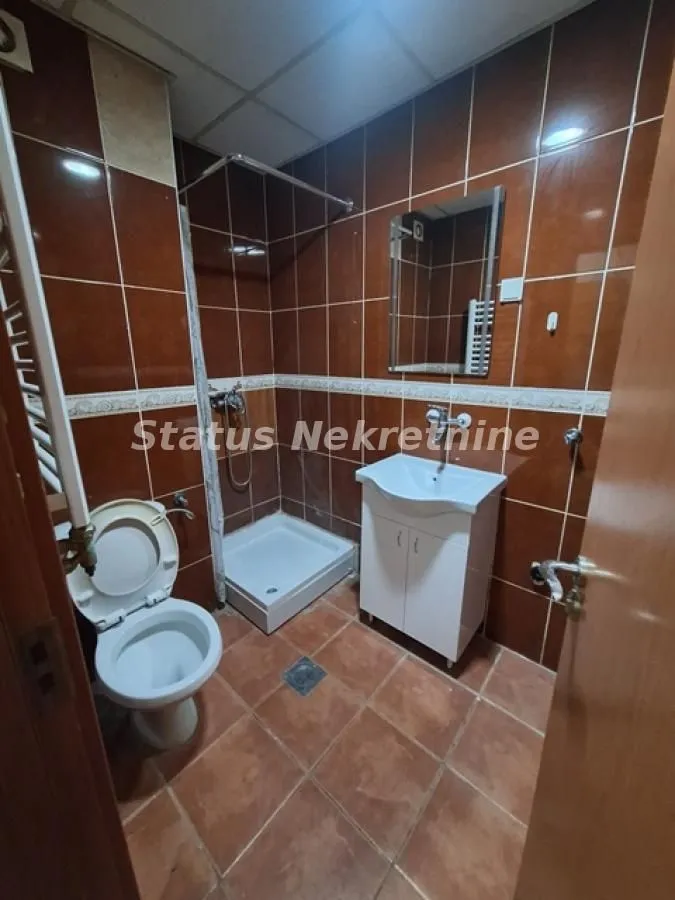 Kupatilo obloženo smeđim pločicama sa tuš kabinom, umivaonikom i toaletom.