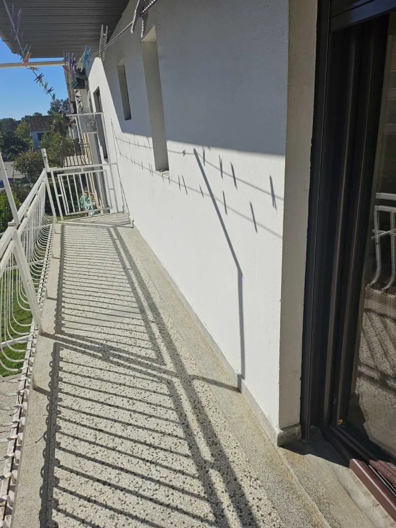 Uski spoljni balkon sa metalnom ogradom obasjan suncem.