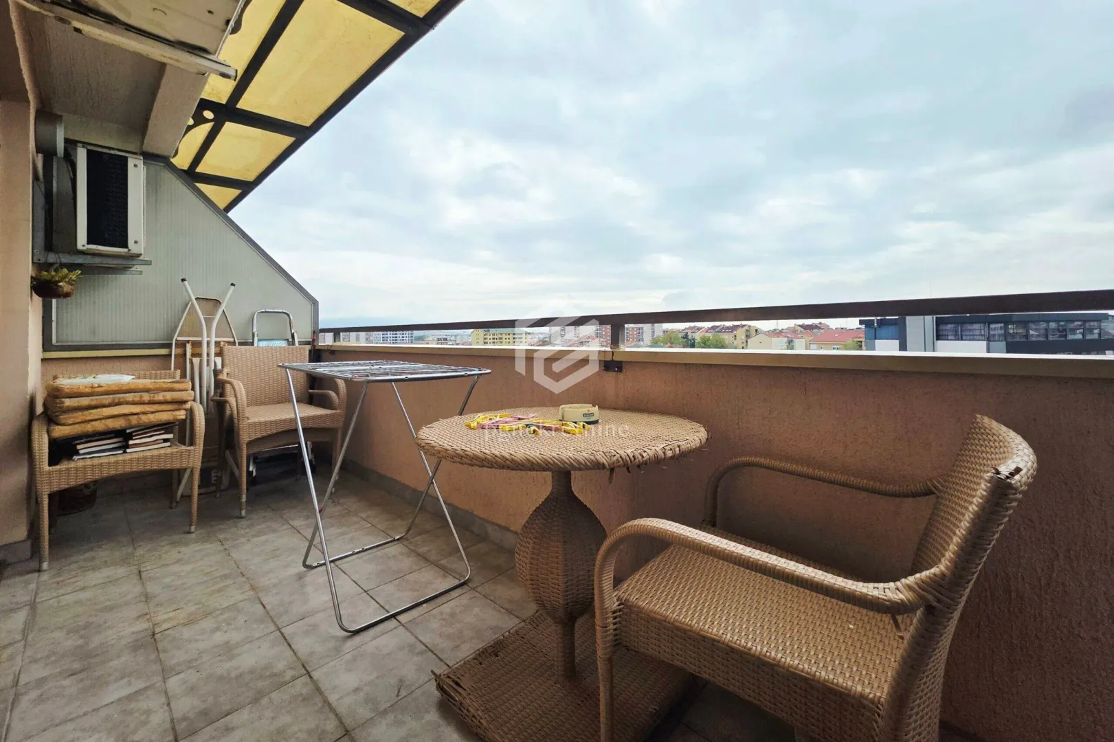 Natkriveni balkon sa pletenim namještajem i pogledom na grad.