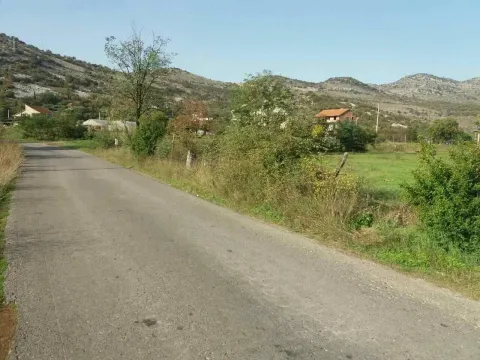 Asfaltni put pored placa sa kućama i brjegovima u pozadini. - image 7