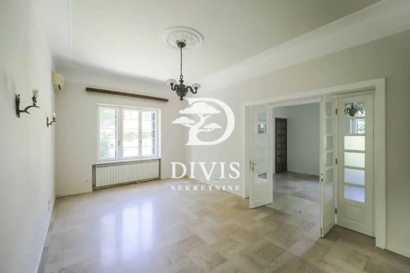 Spacious empty room with light walls, a window, and double doors leading to another room.