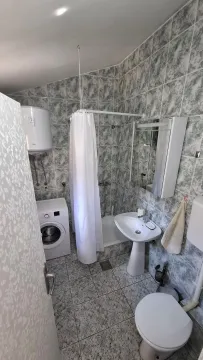 Small bathroom with a shower, washbasin, toilet, and washing machine. - image 7
