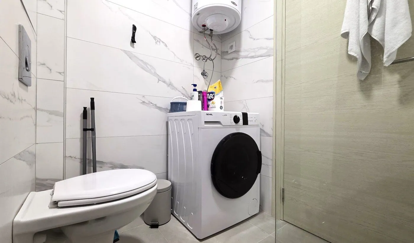 Small bathroom with a washing machine, toilet, and water heater.