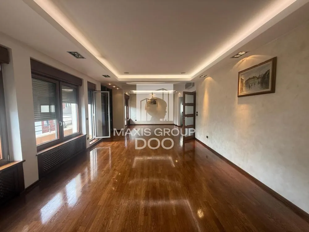 Spacious empty living room with wooden flooring and a drop ceiling with lighting.