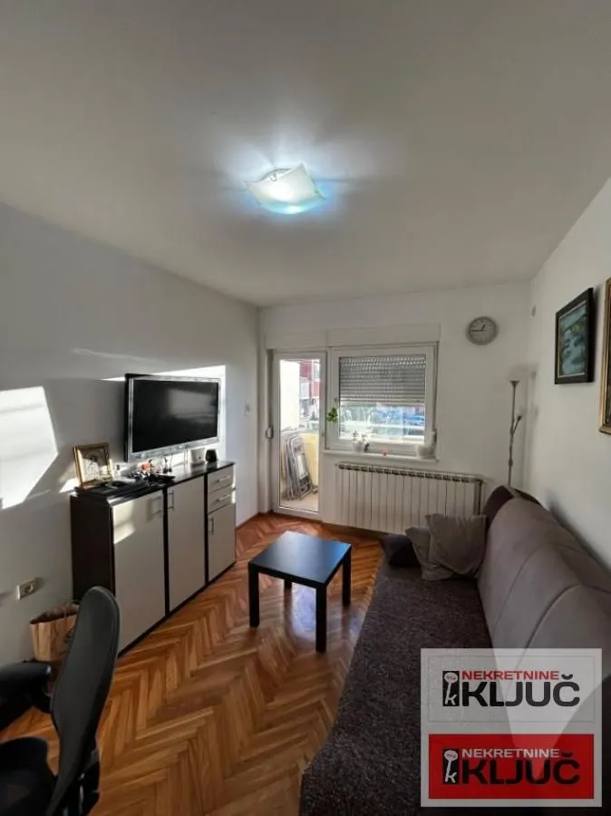 Dnevna soba sa garniturom, televizorom i izlazom na balkon.