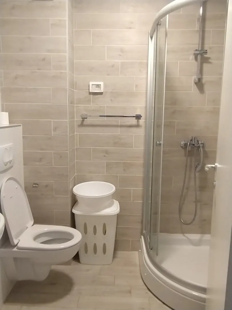 Bright bathroom featuring a shower cabin, toilet, and neutral tiling.