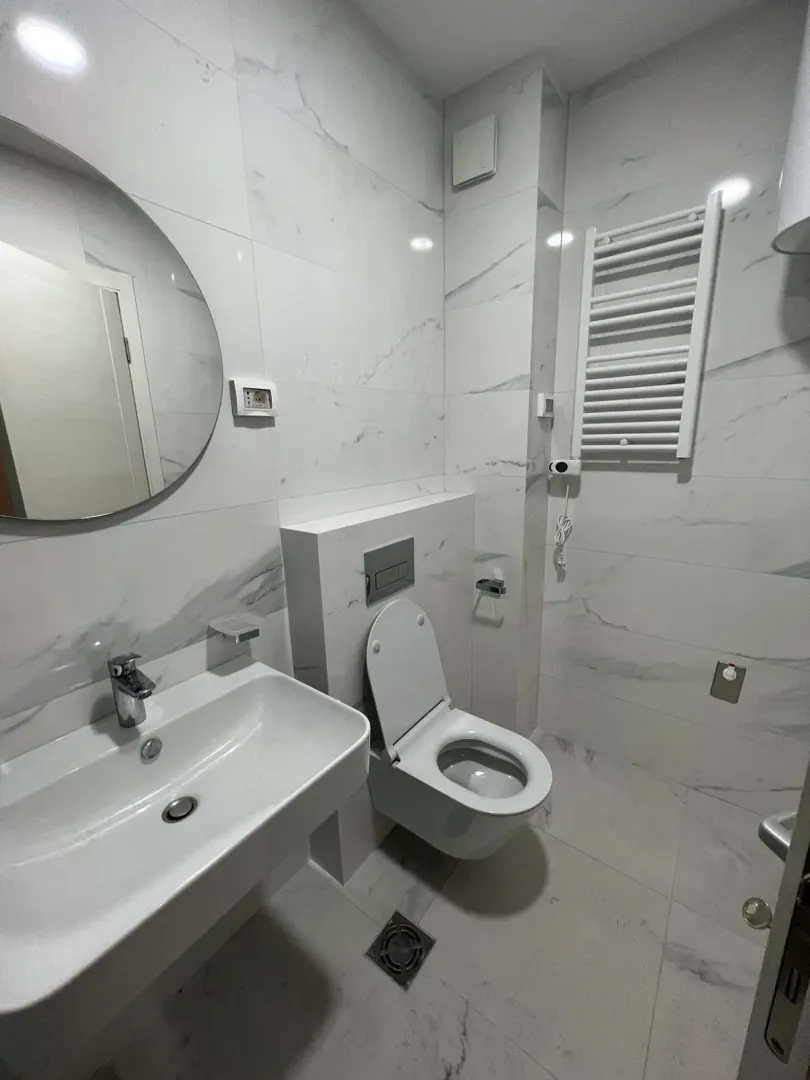Modern bathroom with bright marble tiles and a round mirror.