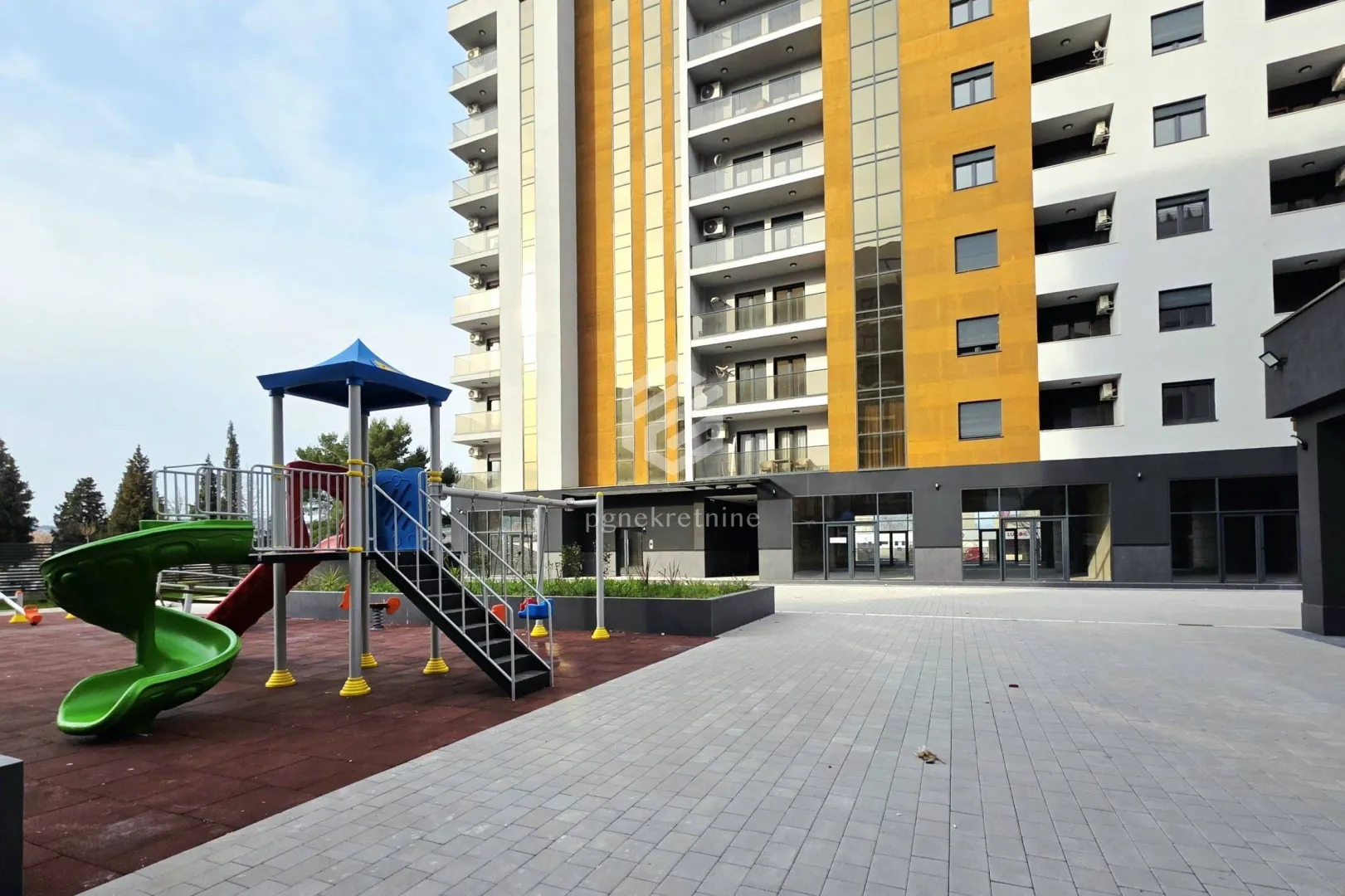 Pogled na modernu stambenu zgradu sa dječijim igralištem u dvorištu.