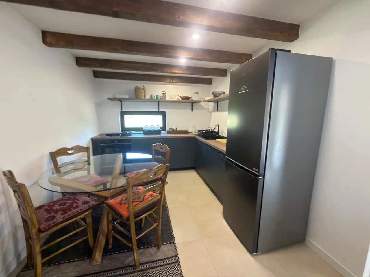 Kitchen equipped with dark cabinets and wooden ceiling beams, featuring a dining table.