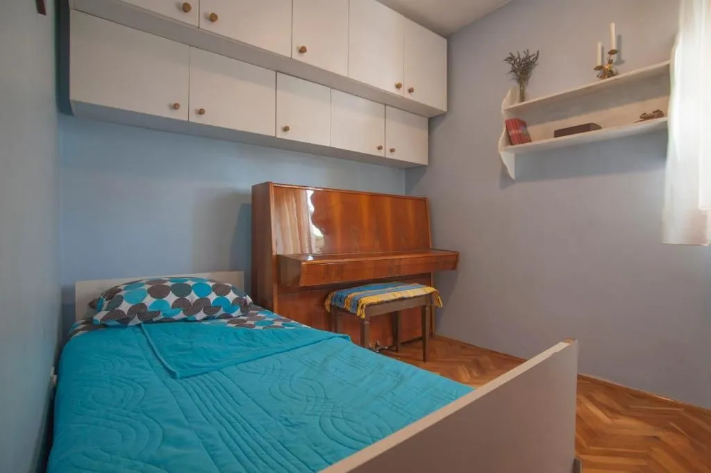 Small bedroom with a bed, piano, and wall-mounted cabinets.