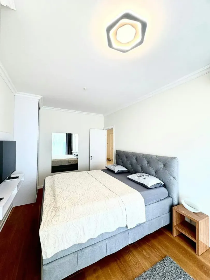 Furnished bedroom with a double bed, white furniture, and wooden flooring.