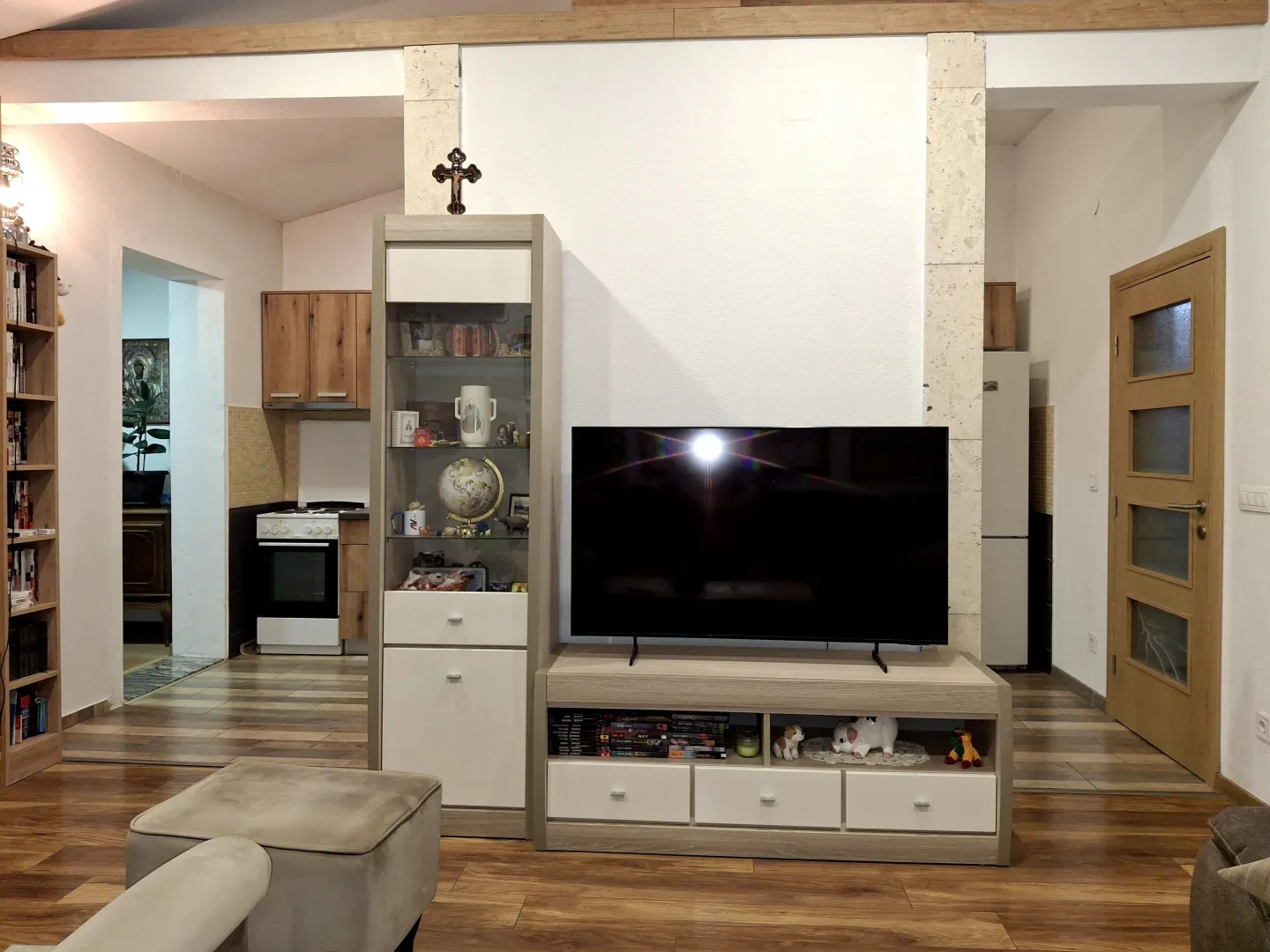 Dnevni boravak sa TV komodom, vitrinom i pogledom na kuhinju i hodnik.