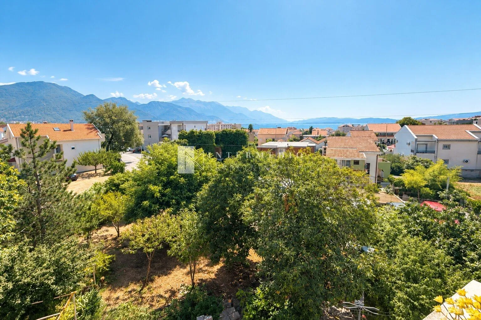 Pogled na okolna naselja, zelenilo i planine u daljini.