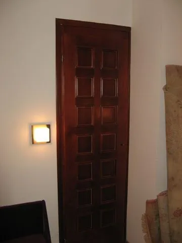 Wooden interior door with decorative panels and a lit wall lamp.